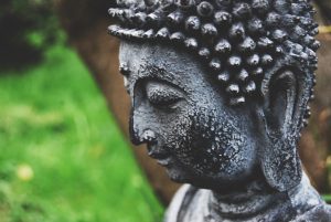 La imágen se observa una estatua de un Buda sobre un fondo verde. Naturaleza y meditación.